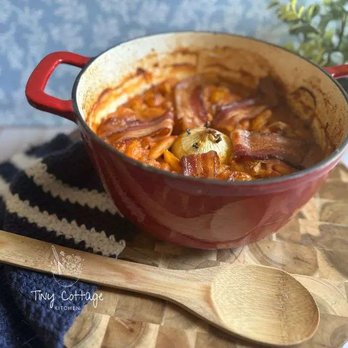 baked lima beans with bacon in a red casserole dish and wooden spoon next to it