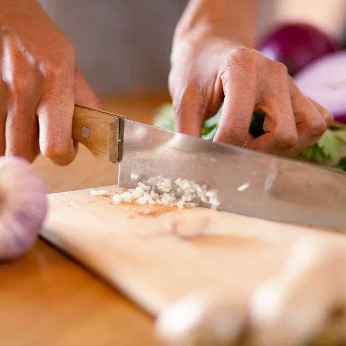 cutting board with hands using a knife to chop garlic