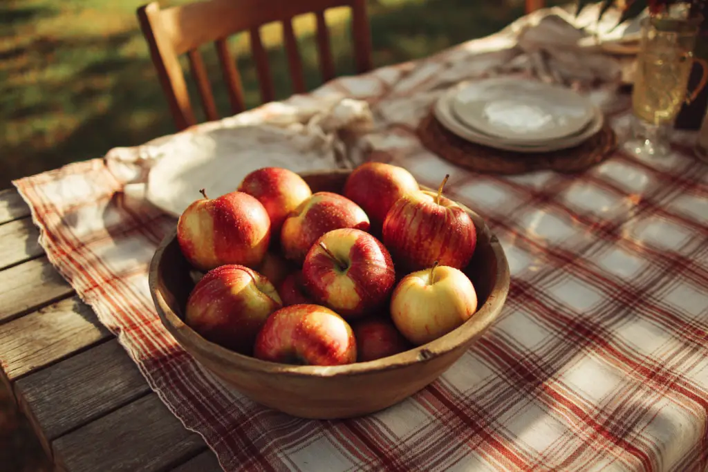 honeycrisp apples in a wood bowl on an outdoor picnic table with gingham tablecloth